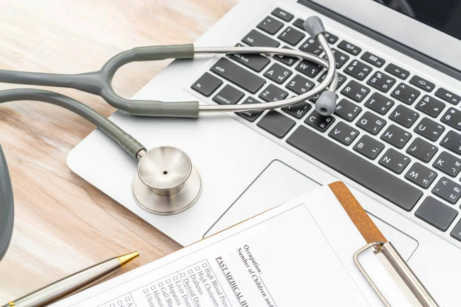 A medical history form, stethoscope and laptop on a desk